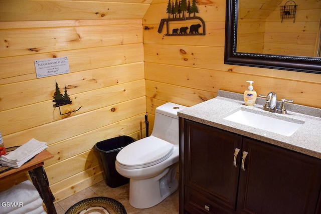 half bathroom featuring wooden walls, vanity, tile patterned flooring, and toilet