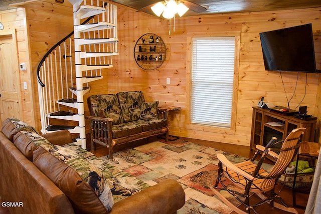 living area with wood walls, stairs, and a ceiling fan