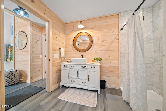 bathroom featuring a tile shower, vanity, wood finished floors, and wooden walls