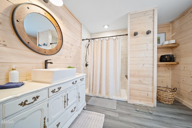 bathroom with wood finished floors, wooden walls, vanity, and tiled shower