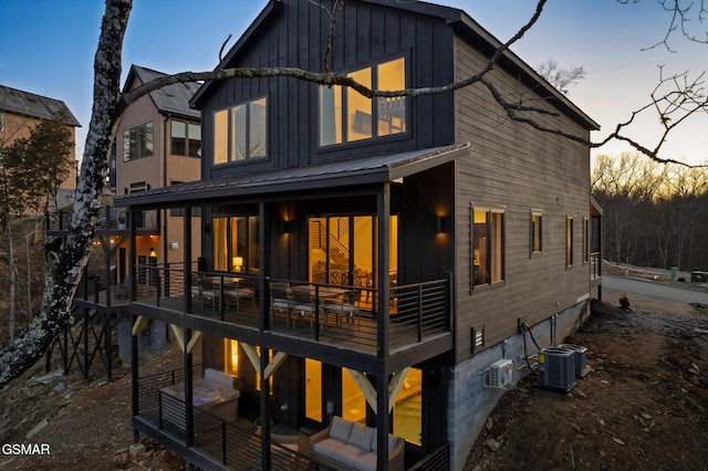 back of property at dusk with board and batten siding, cooling unit, and metal roof