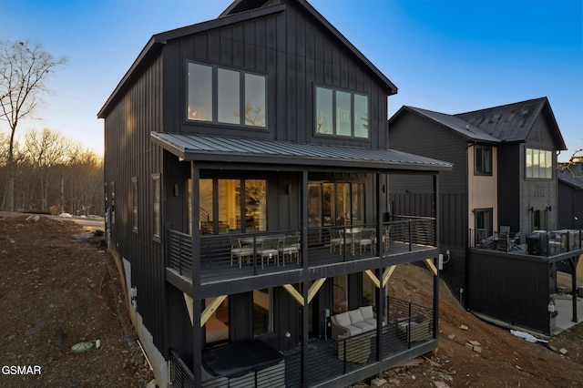 back of house at dusk with a standing seam roof, a wooden deck, board and batten siding, and metal roof