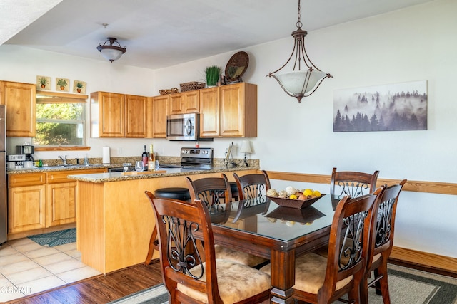 kitchen featuring kitchen peninsula, light stone counters, stainless steel appliances, hanging light fixtures, and light tile patterned flooring