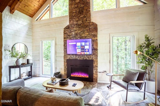 living room featuring wood-type flooring, high vaulted ceiling, plenty of natural light, and a stone fireplace