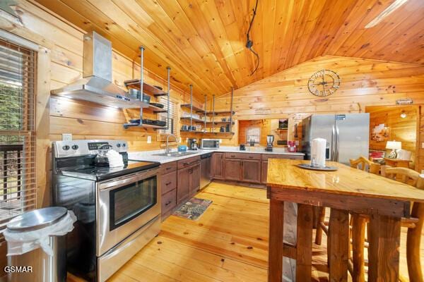 kitchen featuring lofted ceiling, sink, wooden walls, stainless steel appliances, and ventilation hood