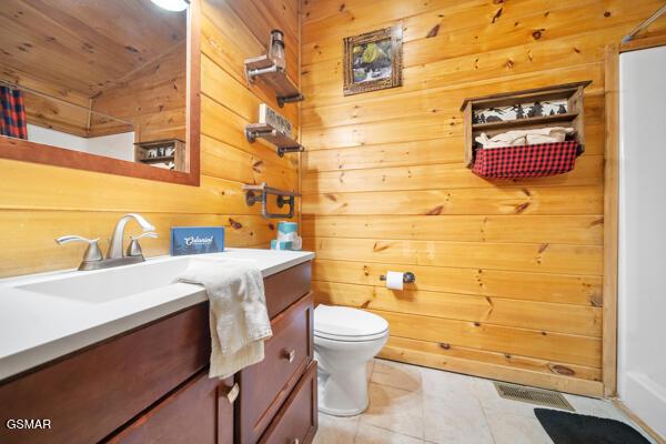 bathroom featuring vanity, wooden walls, tile patterned floors, and toilet