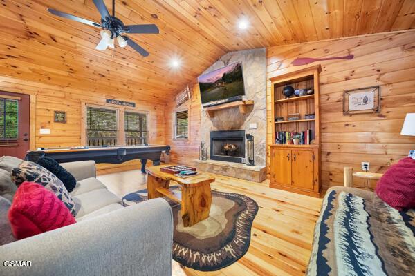 living room featuring wood ceiling, wooden walls, an outdoor stone fireplace, and hardwood / wood-style flooring