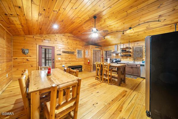 dining room featuring lofted ceiling, wooden walls, wood ceiling, and light hardwood / wood-style flooring