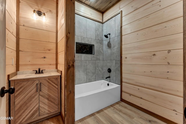 bathroom featuring wood walls, vanity, tiled shower / bath combo, and hardwood / wood-style flooring