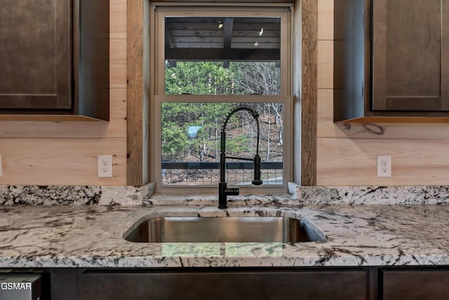 kitchen featuring light stone countertops, dark brown cabinetry, and sink