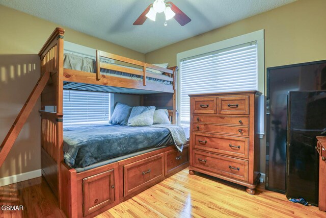 bedroom with a textured ceiling, multiple windows, light wood-style floors, and ceiling fan