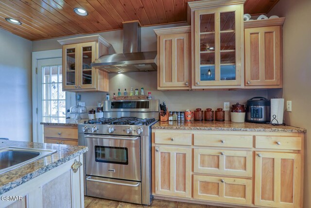 kitchen featuring stainless steel gas stove, light brown cabinetry, a sink, wall chimney exhaust hood, and wooden ceiling