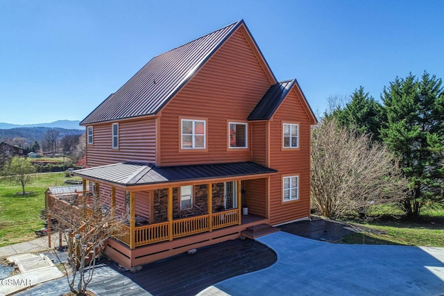 rear view of property featuring log veneer siding, a standing seam roof, covered porch, a mountain view, and metal roof