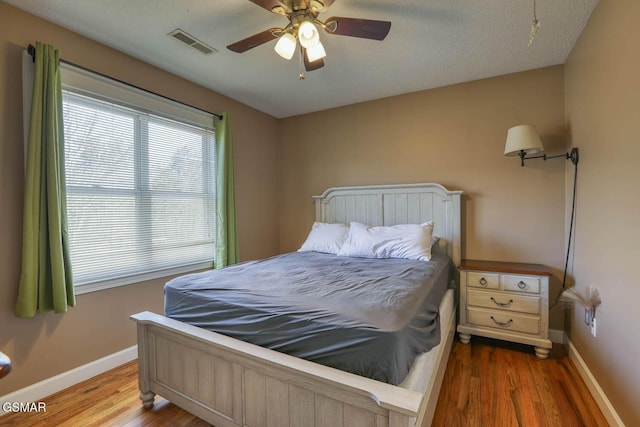 bedroom with ceiling fan, visible vents, baseboards, and wood finished floors