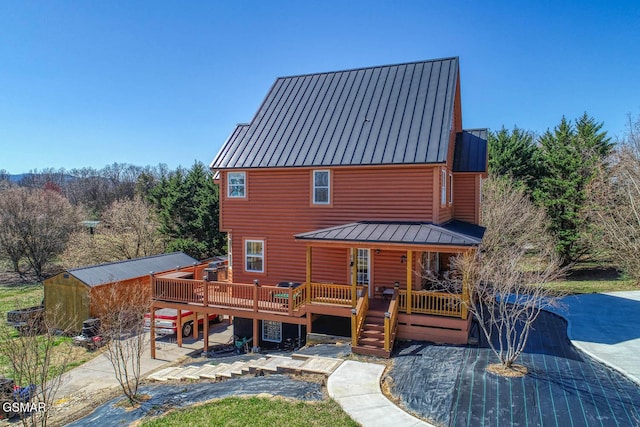 back of house with metal roof, a wooden deck, faux log siding, and a standing seam roof