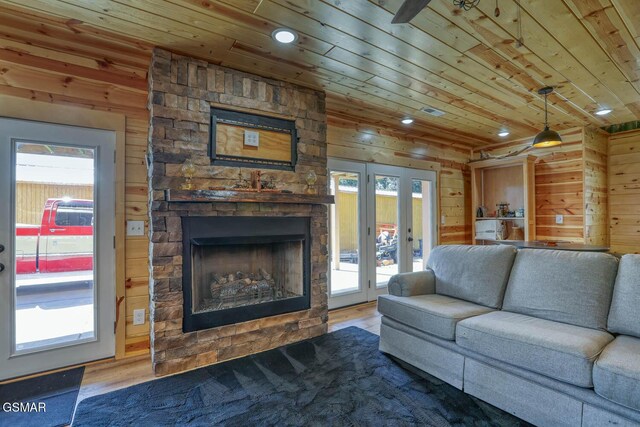 living room featuring a stone fireplace, wooden ceiling, wooden walls, and wood finished floors