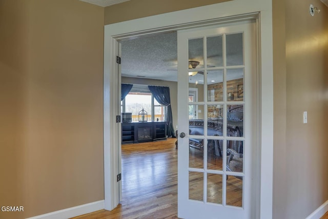 hallway featuring wood finished floors, baseboards, and a textured ceiling