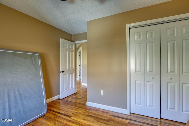 unfurnished bedroom featuring a closet, a textured ceiling, baseboards, and wood finished floors