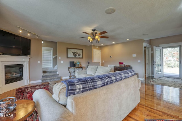 living area with baseboards, stairway, wood finished floors, a glass covered fireplace, and a textured ceiling