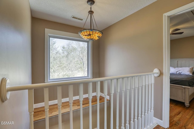 hallway featuring a textured ceiling, wood finished floors, visible vents, and baseboards