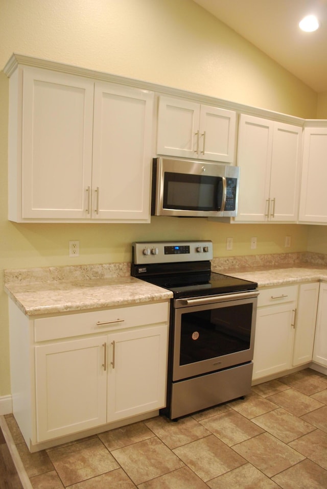 kitchen featuring white cabinets, light stone countertops, stainless steel appliances, and vaulted ceiling