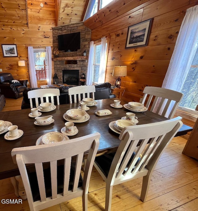 dining room featuring a stone fireplace, wood walls, plenty of natural light, and light wood-type flooring