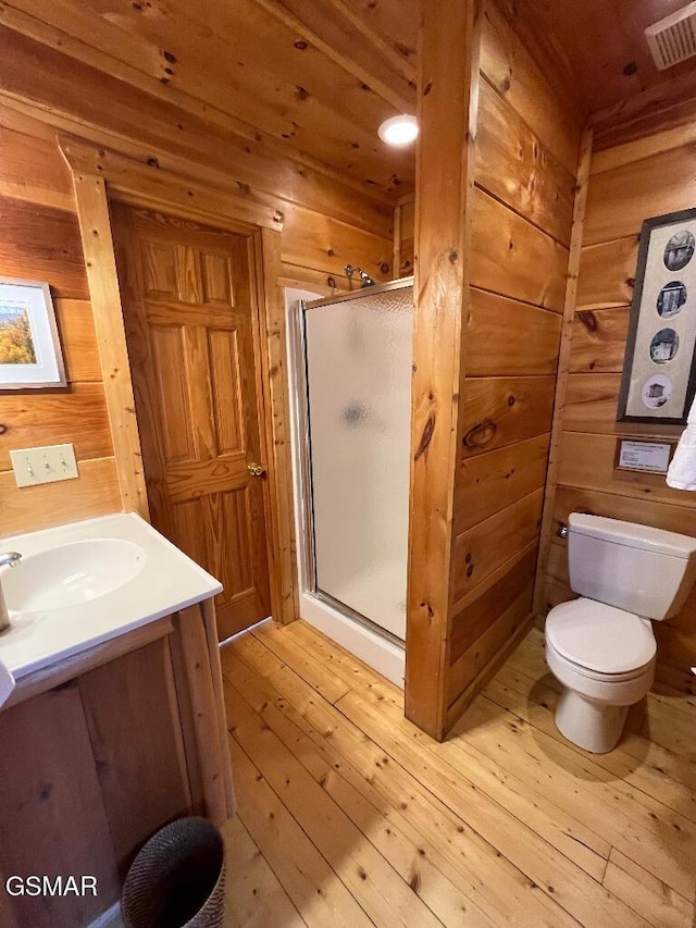 bathroom with vanity, wood-type flooring, a shower with door, and wooden walls