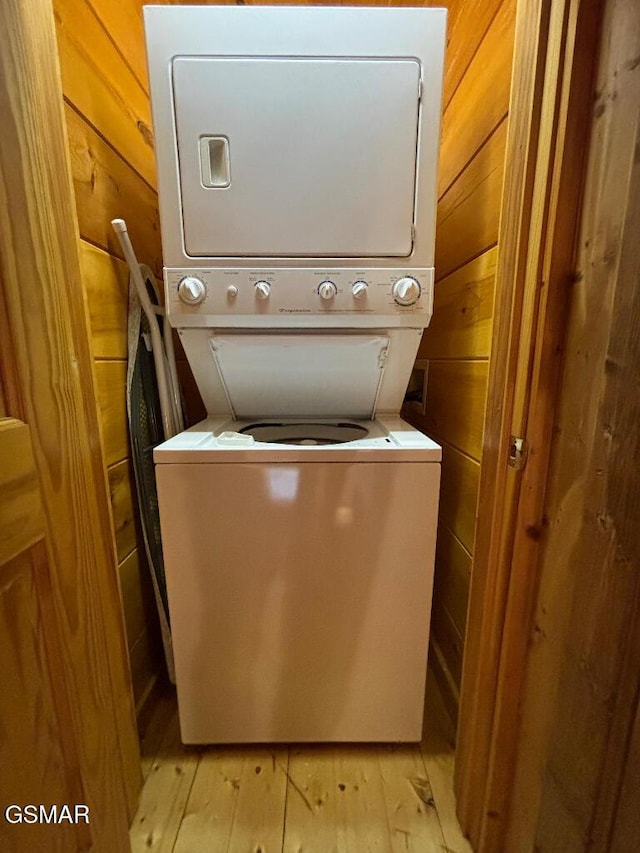 laundry room with wood walls, stacked washing maching and dryer, and light hardwood / wood-style flooring