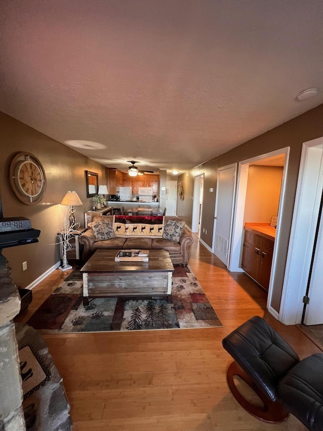 living room featuring ceiling fan, light hardwood / wood-style flooring, and a textured ceiling