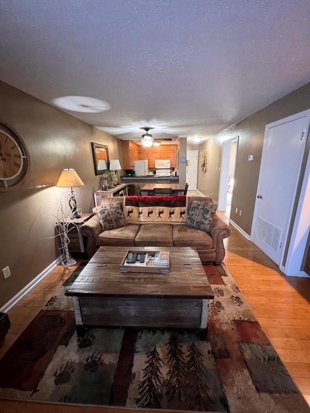 living room featuring ceiling fan, a textured ceiling, and light wood-type flooring