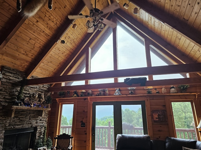 living room with lofted ceiling with beams, ceiling fan, a stone fireplace, and wood ceiling