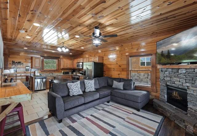 living room with wood walls, ceiling fan with notable chandelier, light tile patterned floors, a fireplace, and wood ceiling