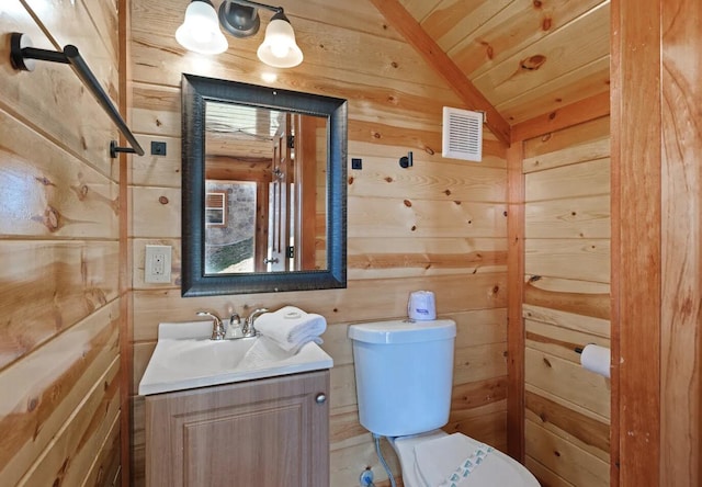 bathroom with wood walls, vanity, lofted ceiling, and toilet