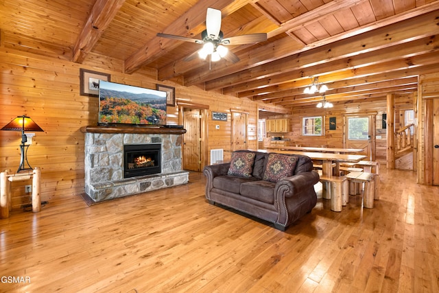 living room with beamed ceiling, a stone fireplace, wooden walls, and wood ceiling