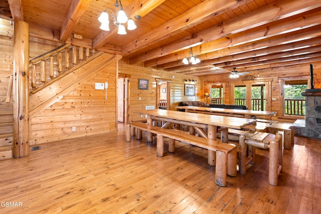 dining space featuring ceiling fan with notable chandelier, light wood-type flooring, rustic walls, beam ceiling, and wood ceiling