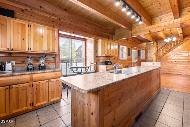 kitchen featuring sink, a center island with sink, an inviting chandelier, wood walls, and light tile patterned flooring