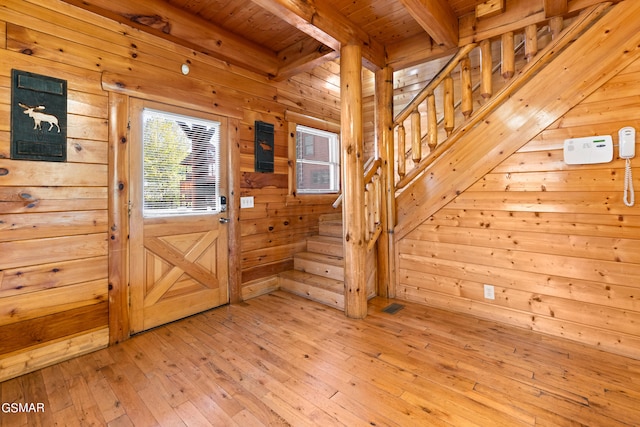 foyer featuring light wood-type flooring, wooden ceiling, and wood walls