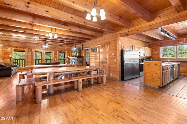 kitchen with wooden walls, beam ceiling, appliances with stainless steel finishes, and light hardwood / wood-style flooring