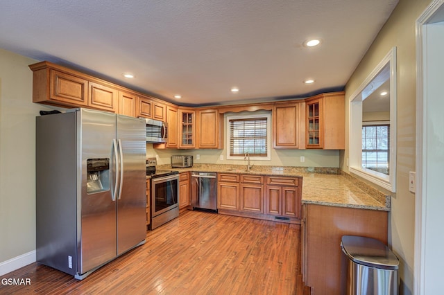 kitchen featuring light hardwood / wood-style floors, light stone counters, appliances with stainless steel finishes, and a healthy amount of sunlight