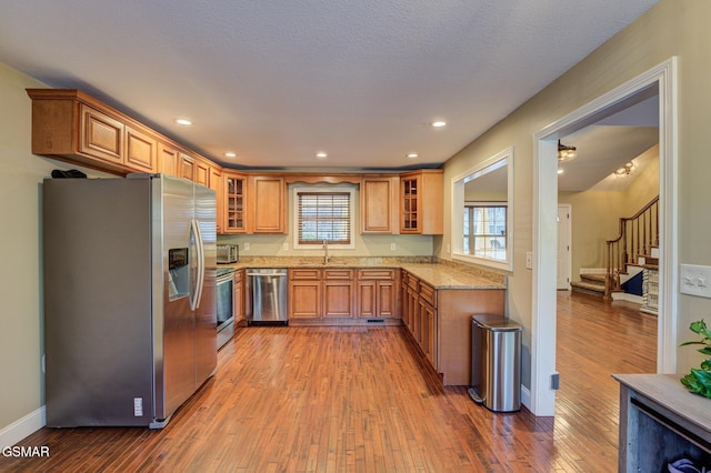 kitchen featuring sink, hardwood / wood-style flooring, a textured ceiling, stainless steel appliances, and light stone counters