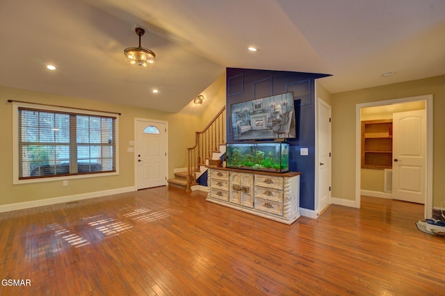 unfurnished living room with lofted ceiling, hardwood / wood-style floors, stairway, and baseboards