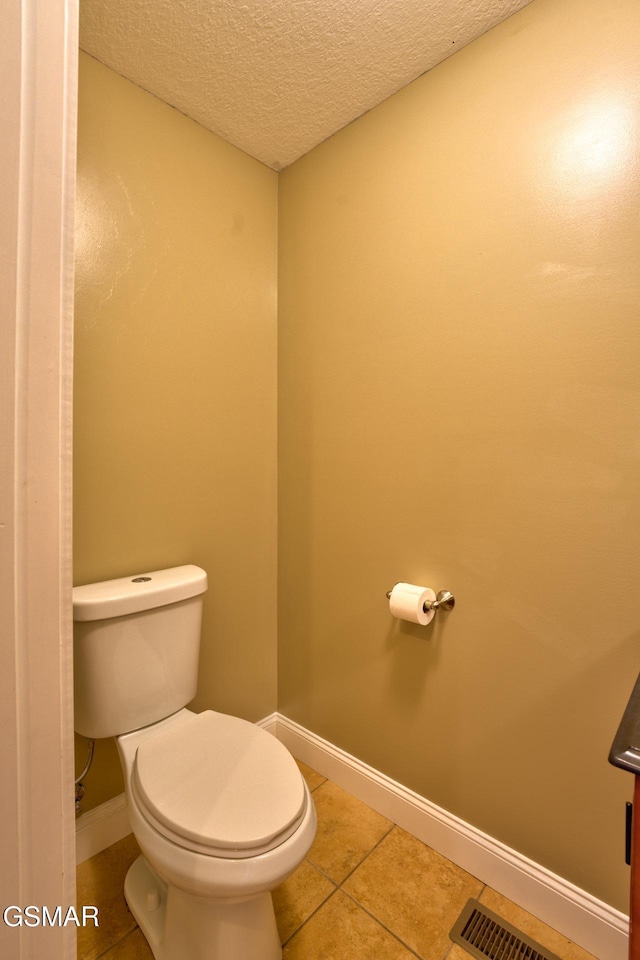 bathroom with visible vents, toilet, a textured ceiling, baseboards, and tile patterned floors