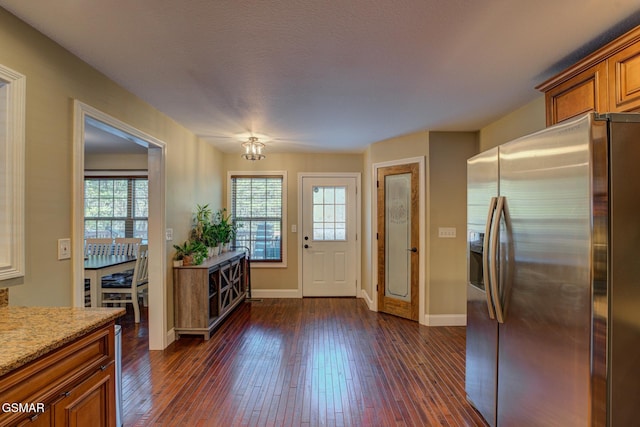 kitchen featuring light stone countertops, baseboards, stainless steel fridge with ice dispenser, brown cabinets, and dark wood-style floors