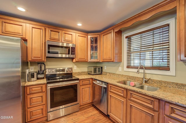 kitchen featuring light stone counters, sink, appliances with stainless steel finishes, and light wood-type flooring