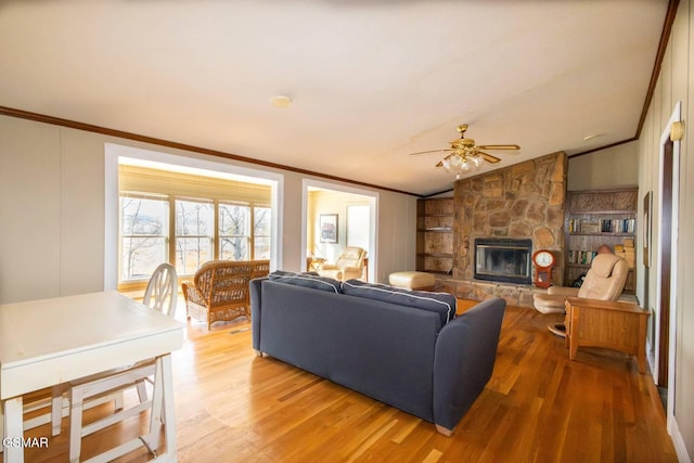 living room with ornamental molding, ceiling fan, light hardwood / wood-style flooring, a stone fireplace, and lofted ceiling