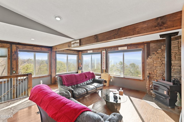 living area featuring a wood stove, hardwood / wood-style flooring, vaulted ceiling, and a textured ceiling