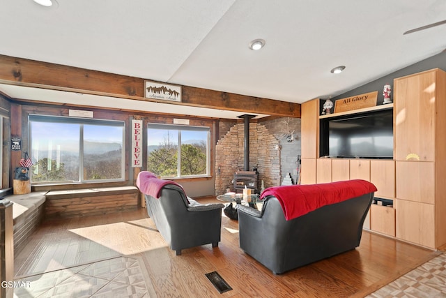 living room with lofted ceiling with beams, a wood stove, wood finished floors, and visible vents