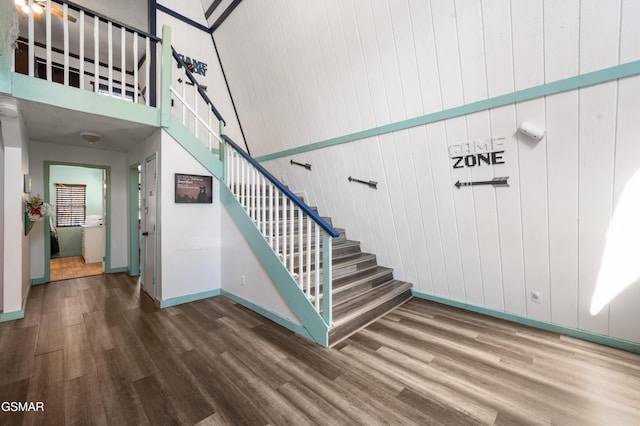 stairway featuring wood-type flooring, a towering ceiling, and wooden walls