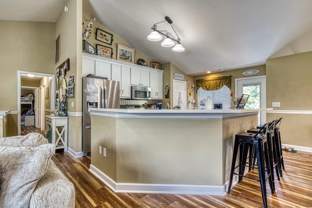 kitchen with vaulted ceiling, a breakfast bar area, stainless steel appliances, decorative backsplash, and white cabinetry