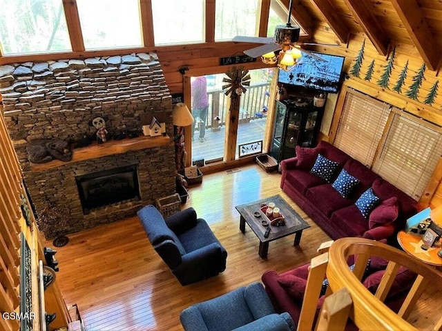 living room with ceiling fan, plenty of natural light, a stone fireplace, and hardwood / wood-style floors